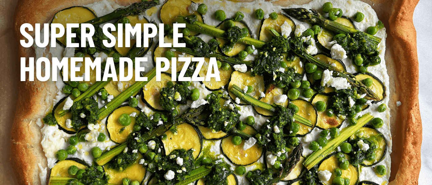 A top-down view of a rectangular pizza topped with feta, ricotta, asparagus, courgette, green peas, and parmesan.