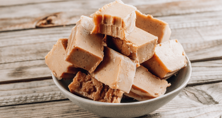 A bowl of rich fudge placed on a rustic wooden table, showcasing its smooth texture and inviting appearance.