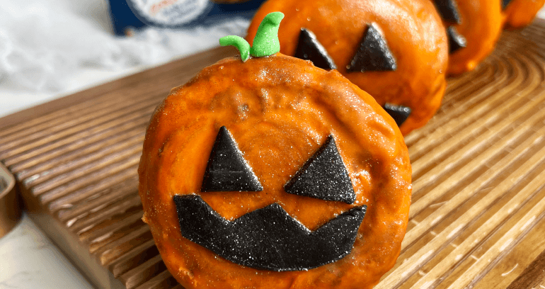 A festive display of round pumpkin croissant featuring playful icing faces, perfect for Halloween celebrations.