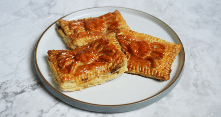 Three chocolate and strawberry spider pastry slices, elegantly arranged on a white plate.