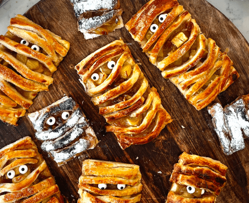 A wooden tray adorned with Halloween mummy pastry pies filled with delicious apple and fudge filling.