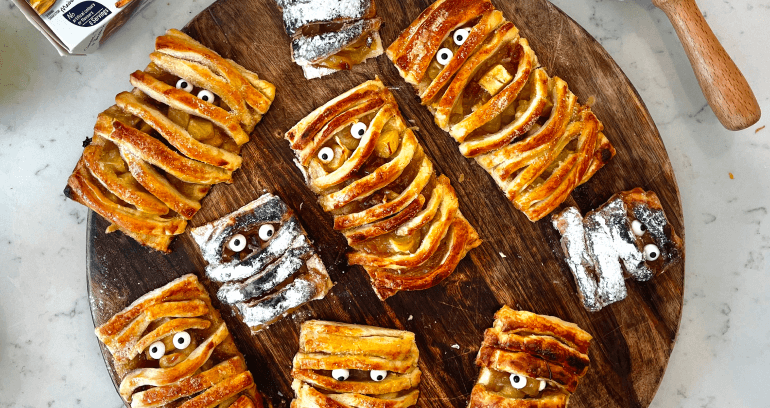 A wooden tray adorned with Halloween mummy pastry pies filled with delicious apple and fudge filling.