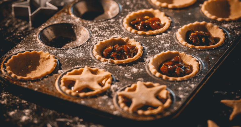 A baking pan filled with an assortment of festive mince pies, showcasing a variety of fillings and pie tops for decoration.