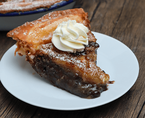 A slice of brown sugar cookie pie topped with cream served on a white plate on a wooden table.