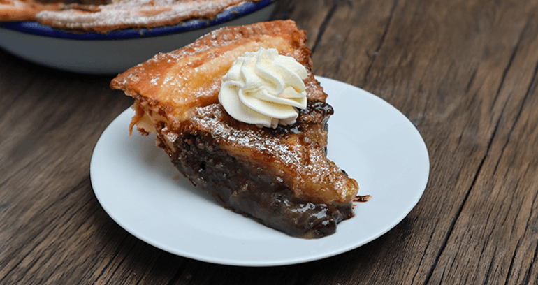 A slice of brown sugar cookie pie topped with cream served on a white plate on a wooden table.