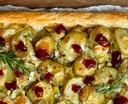 A rectangular tart topped with sliced potatoes, leeks, and brie on a flaky pastry crust.