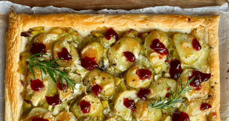 A rectangular tart topped with sliced potatoes, leeks, and brie on a flaky pastry crust.