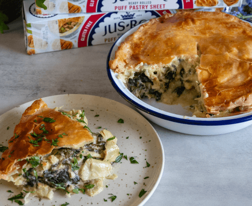 A round, golden, Spinach and Artichoke pie served on a plate with a box of Jus-Rol puff pastry in the background